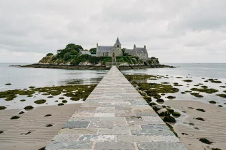 Chaussée pavée menant à l'île de Saint-Cado en Bretagne à marée basse, avec vue sur les maisons en granit et la chapelle romane