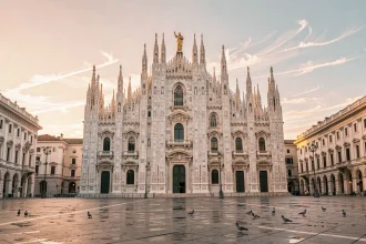 Vue grand angle du Dôme de Milan depuis la Piazza del Duomo au lever du soleil, avec les flèches gothiques se découpant sur un ciel rosé et ambré