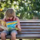 girl in red top sitting on bench while reading