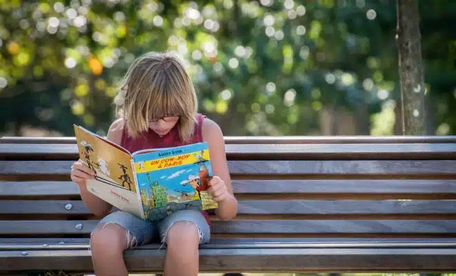 girl in red top sitting on bench while reading